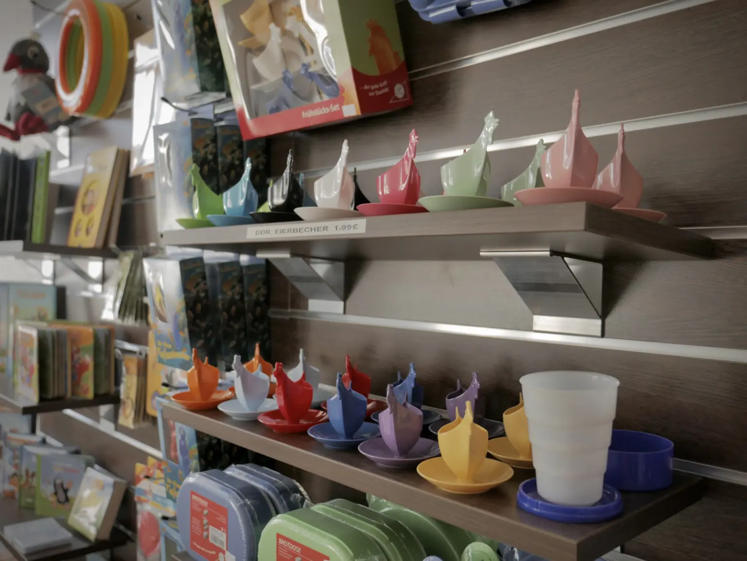 Bunte Hühner-Eierbecher im DDR-Design, aufgereiht auf Wandregalen