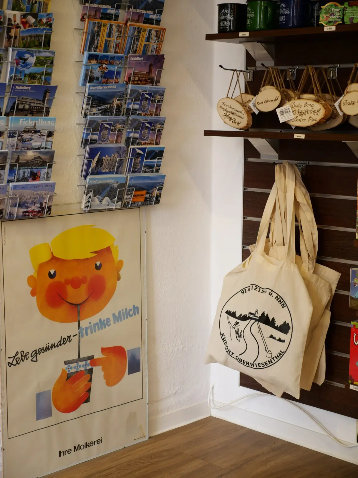 Ständer mit Ansichtskarten aus Oberwiesenthal und vom Fichtelberg, Stoffbeutel mit Aufdruck „Kurort Oberwiesenthal“, Holzanhänger und ein Retro-Plakat „Lebe gesünder – trinke Milch“