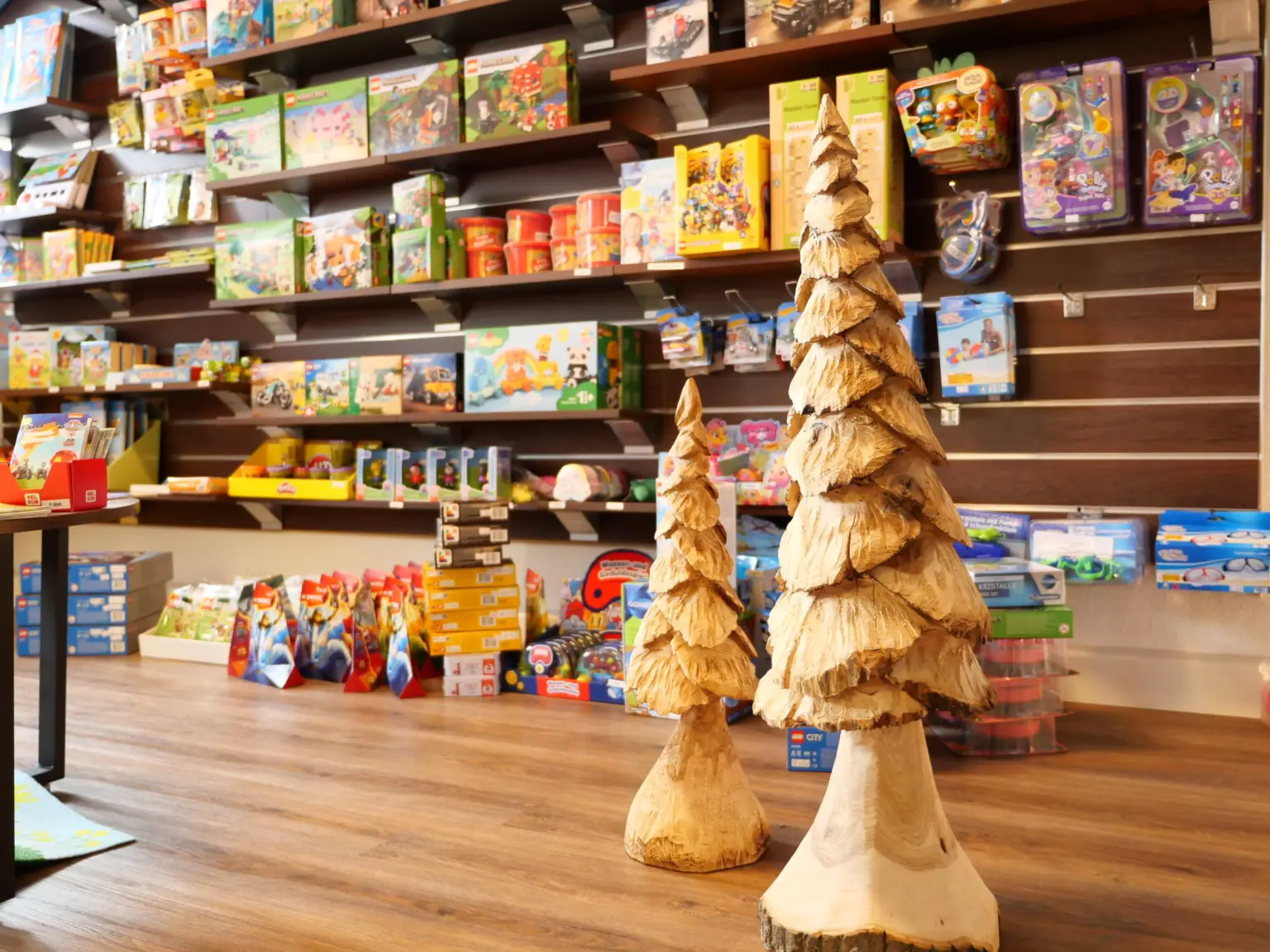 Spielwarenabteilung im Laden am Markt mit vollen Regalen voller Spielzeug, im Vordergrund zwei aus Holz geschnitzte Tannen